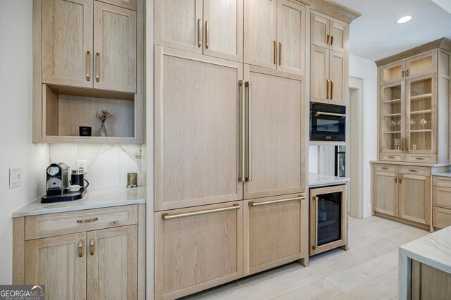 kitchen with paneled refrigerator, oven, light brown cabinetry, wine cooler, and light stone countertops