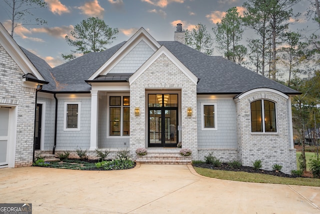 view of front of house featuring driveway, brick siding, roof with shingles, and a chimney