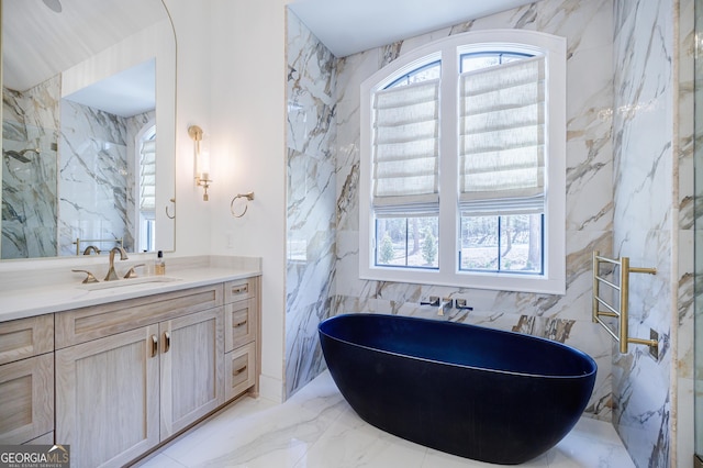 bathroom featuring a wealth of natural light, a freestanding bath, marble finish floor, and vanity