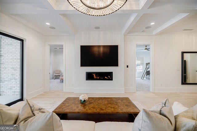 living room with beam ceiling, a warm lit fireplace, coffered ceiling, and a chandelier