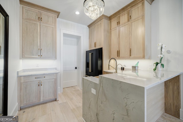 kitchen with light stone countertops, light wood finished floors, a peninsula, light brown cabinetry, and black fridge with ice dispenser