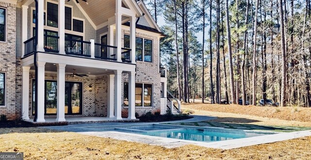 back of property with a ceiling fan, a patio, a balcony, an outdoor pool, and brick siding