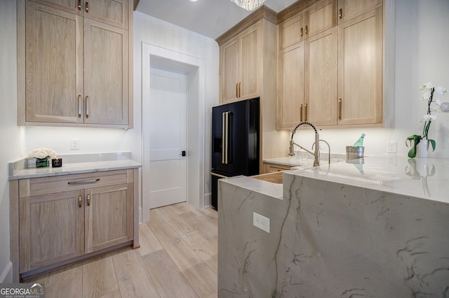 kitchen featuring light brown cabinets, light stone countertops, a sink, light wood-style floors, and black fridge with ice dispenser