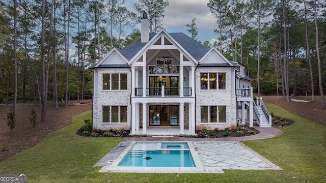 back of house featuring a standing seam roof, a balcony, a lawn, and brick siding