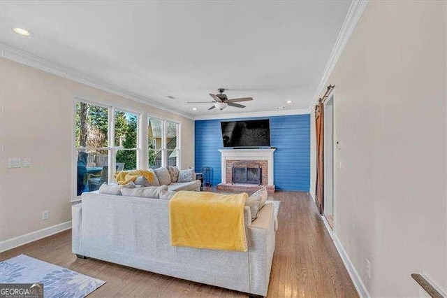 living area featuring baseboards, a brick fireplace, wood finished floors, and crown molding