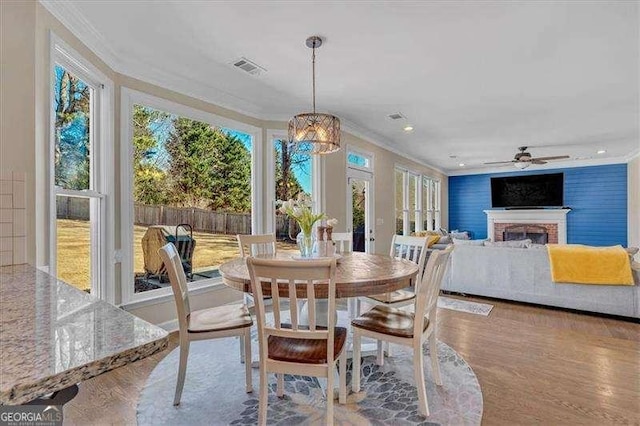 dining area with a fireplace, visible vents, crown molding, and wood finished floors