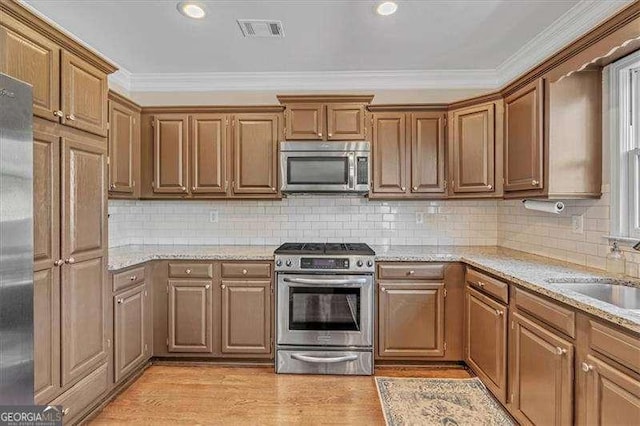 kitchen with light wood finished floors, visible vents, appliances with stainless steel finishes, ornamental molding, and a sink