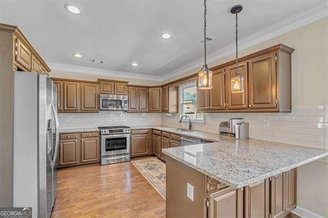 kitchen featuring a peninsula, a sink, light wood-style floors, appliances with stainless steel finishes, and crown molding