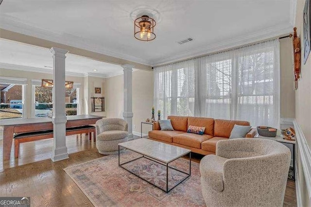 living area with wood finished floors, visible vents, baseboards, ornate columns, and crown molding