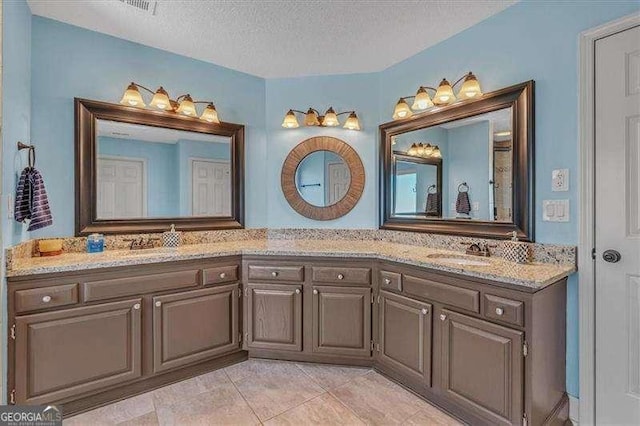 bathroom featuring double vanity, a textured ceiling, a sink, and tile patterned floors