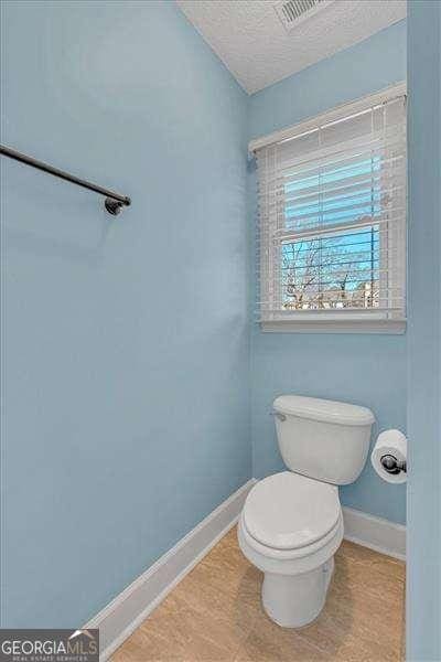 bathroom with visible vents, toilet, a textured ceiling, and baseboards