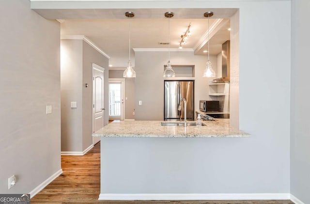 kitchen with freestanding refrigerator, a sink, wood finished floors, a peninsula, and wall chimney exhaust hood