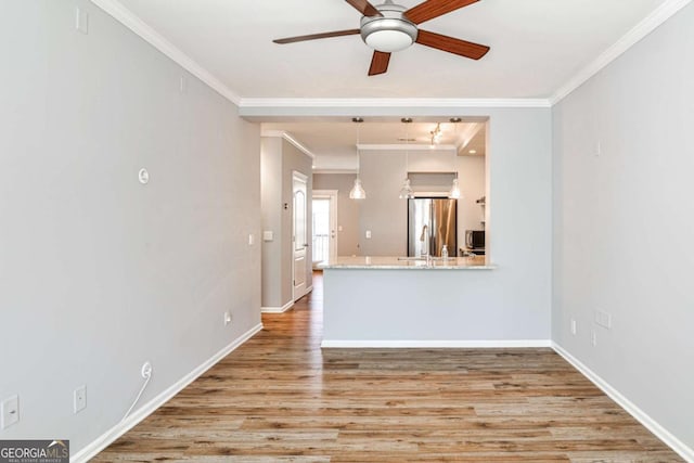 interior space with a ceiling fan, crown molding, baseboards, and wood finished floors