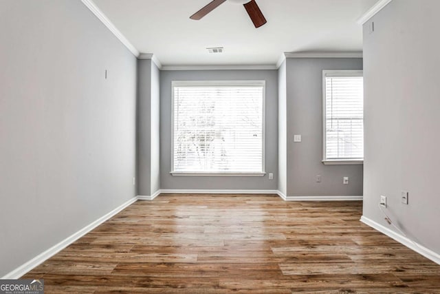 empty room with baseboards, visible vents, crown molding, and wood finished floors