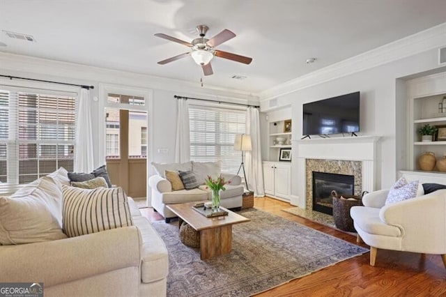 living area with built in shelves, a fireplace, crown molding, and visible vents