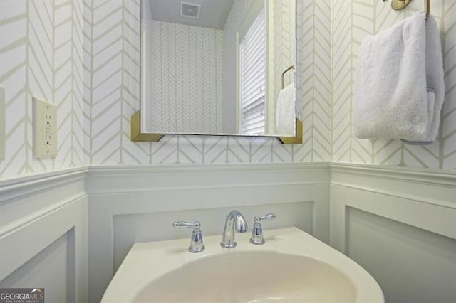 bathroom featuring a wainscoted wall, a sink, visible vents, and wallpapered walls