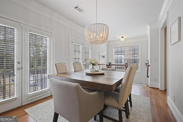 dining space with visible vents, ornamental molding, wood finished floors, french doors, and a chandelier