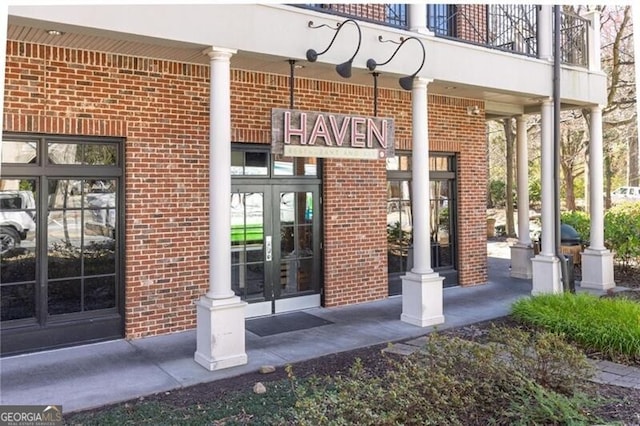 entrance to property with a balcony, brick siding, and french doors