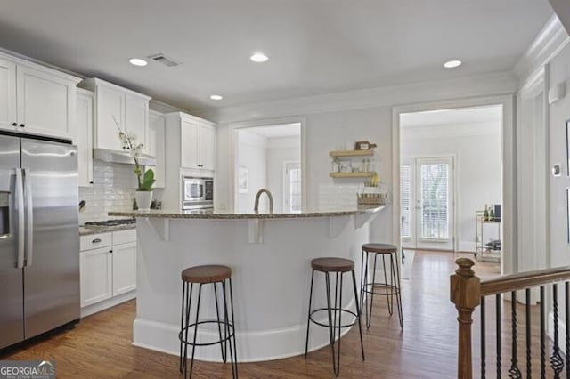 kitchen featuring light stone counters, a breakfast bar, dark wood-style flooring, stainless steel appliances, and white cabinetry