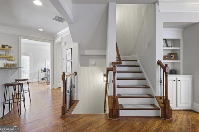 staircase with built in shelves, visible vents, wood finished floors, and ornamental molding