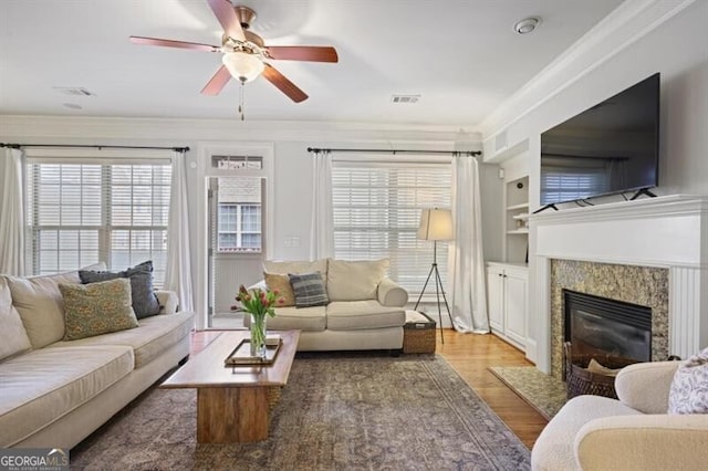 living area featuring crown molding, a premium fireplace, visible vents, and wood finished floors