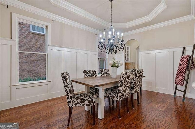 dining room with a notable chandelier, a decorative wall, dark wood-type flooring, and a raised ceiling