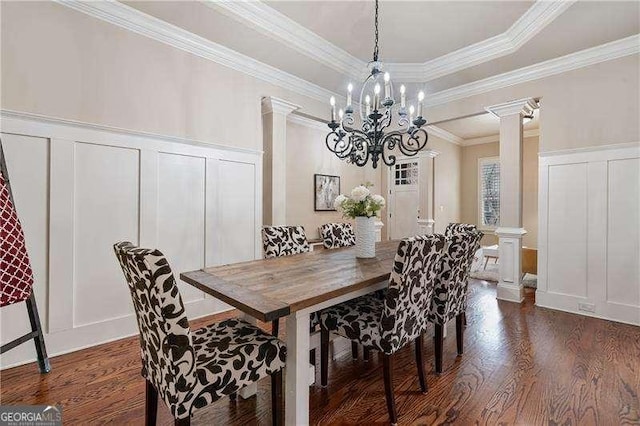 dining area featuring decorative columns, a tray ceiling, a decorative wall, and dark wood finished floors