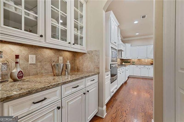 kitchen with light stone counters, visible vents, white cabinets, stainless steel microwave, and glass insert cabinets