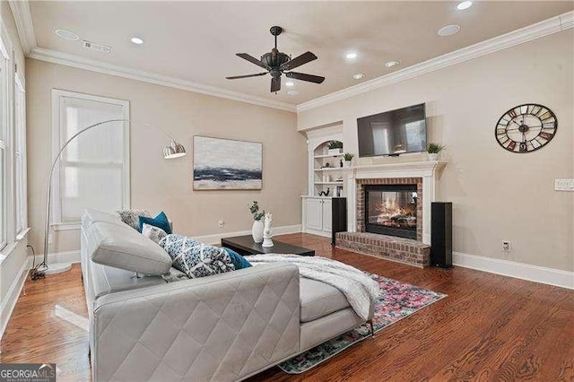 living room featuring visible vents, baseboards, wood finished floors, crown molding, and a brick fireplace