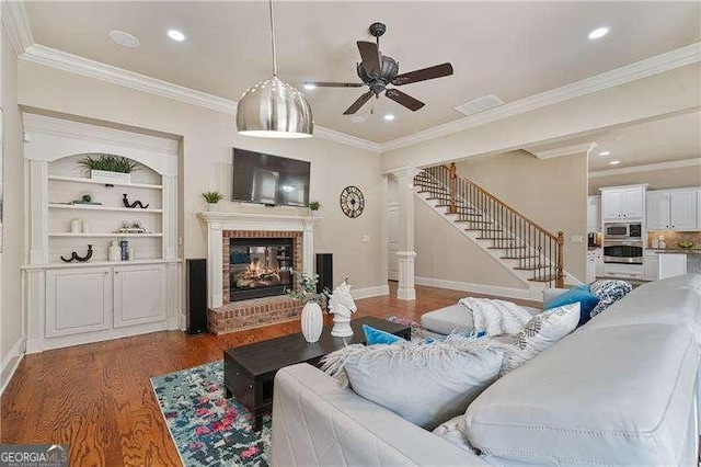 living area with baseboards, stairway, wood finished floors, crown molding, and a brick fireplace