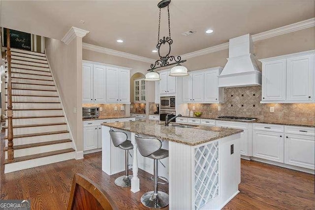 kitchen featuring appliances with stainless steel finishes, white cabinets, custom range hood, and a sink