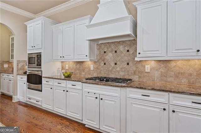 kitchen featuring white cabinetry, premium range hood, appliances with stainless steel finishes, and arched walkways