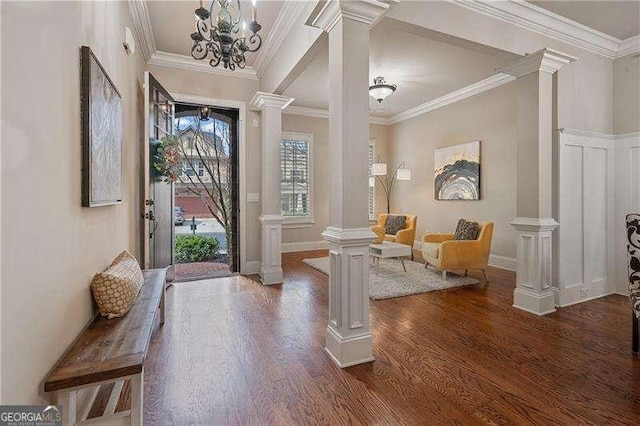 entryway with dark wood-style floors, decorative columns, ornamental molding, and a notable chandelier