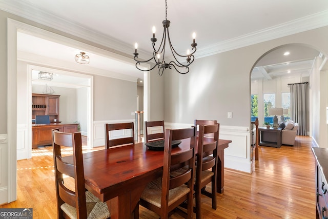 dining space featuring a wainscoted wall, arched walkways, light wood-style floors, crown molding, and a decorative wall