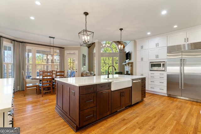 kitchen with a sink, white cabinets, built in appliances, crown molding, and decorative light fixtures