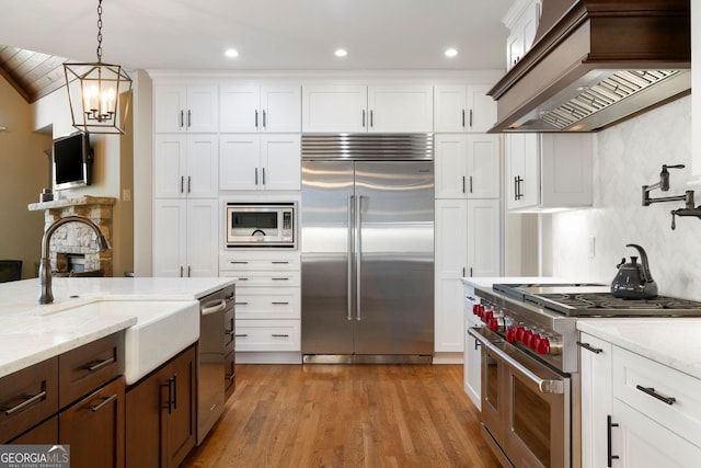 kitchen with white cabinetry, decorative light fixtures, premium range hood, and built in appliances