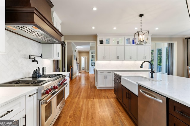 kitchen featuring premium range hood, a sink, white cabinets, glass insert cabinets, and appliances with stainless steel finishes