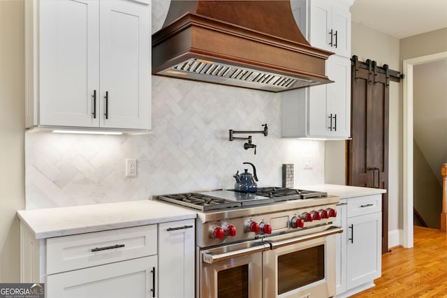 kitchen with backsplash, premium range hood, double oven range, a barn door, and white cabinets