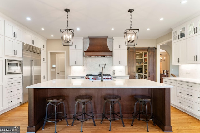 kitchen featuring light countertops, custom range hood, arched walkways, and built in appliances