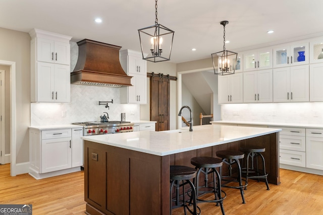 kitchen featuring custom exhaust hood, a barn door, light wood finished floors, and a sink