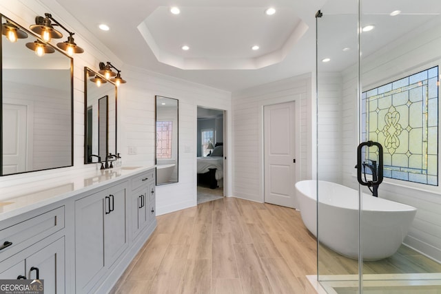 ensuite bathroom featuring a sink, wood finished floors, double vanity, a raised ceiling, and a soaking tub