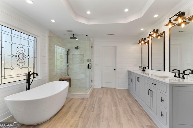 bathroom with a shower stall, double vanity, wood finished floors, a raised ceiling, and a sink