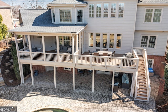 rear view of property featuring stairway, a wooden deck, decorative driveway, and a shingled roof