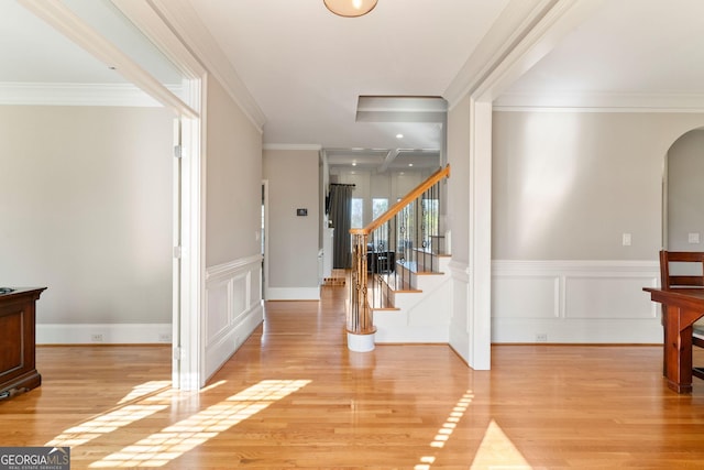 entryway featuring crown molding, stairs, wainscoting, light wood-style flooring, and arched walkways