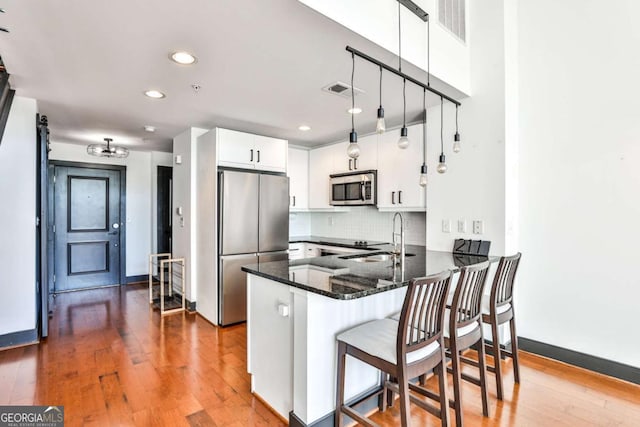 kitchen with stainless steel appliances, a peninsula, a sink, white cabinets, and tasteful backsplash