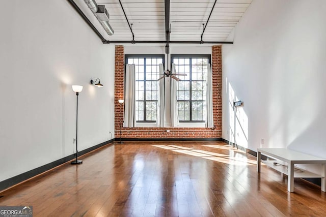 spare room featuring brick wall, baseboards, and hardwood / wood-style floors