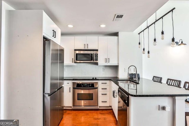 kitchen featuring stainless steel appliances, a peninsula, a sink, visible vents, and backsplash