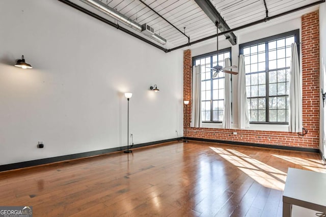 unfurnished room with brick wall, baseboards, wood-type flooring, and beam ceiling