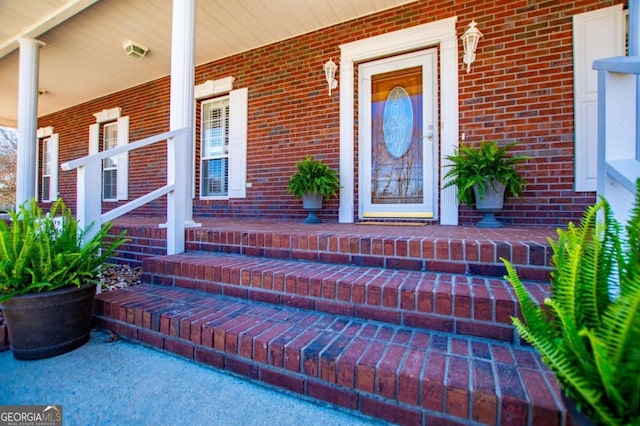 entrance to property featuring covered porch and brick siding