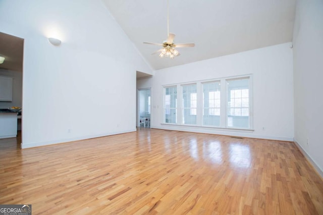 unfurnished living room with ceiling fan, high vaulted ceiling, light wood-style flooring, and baseboards